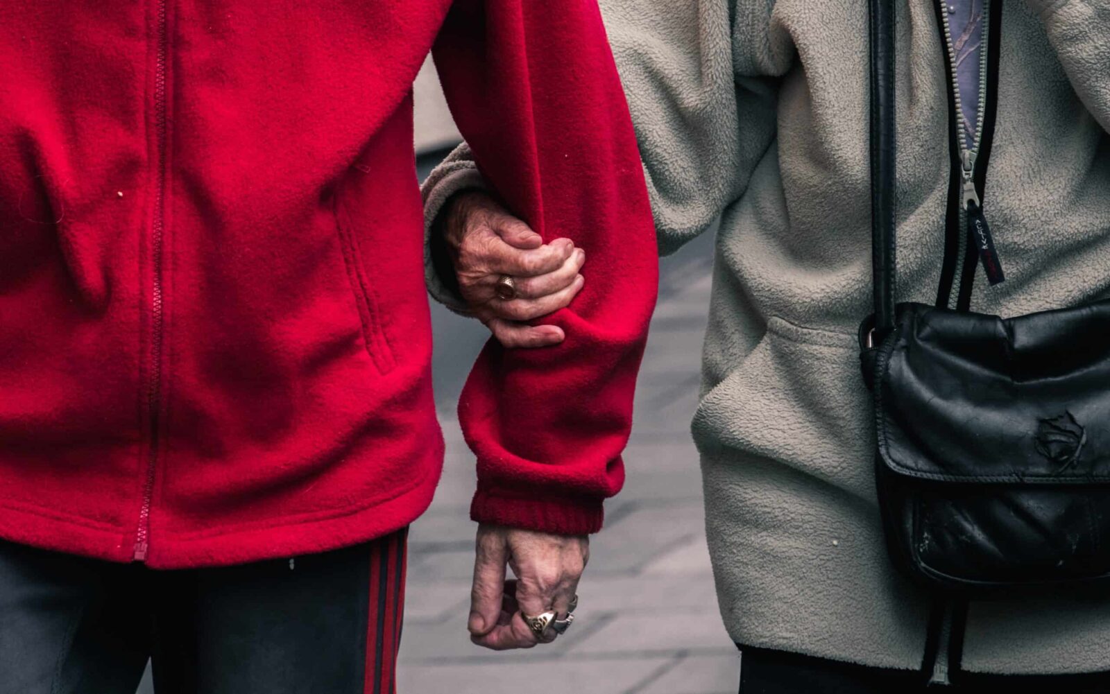 Two elderly ladies in a red and grey jacket. One is supporting the other by holding her arm. Together we can fight the stigma of mental healthcare. Together we all can overcome shame and the stigma of psychiatry and mental healthcare.  