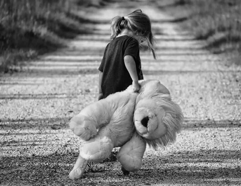 Separation trauma. Black and white picture showing a little girl with a teddy. The girl moves in unknown direction along a country road. She looks lost and despaired. The picture symbolizes Bowlby’s concept of separation stress. John Bowlby was the key figure in the history of PTSD research