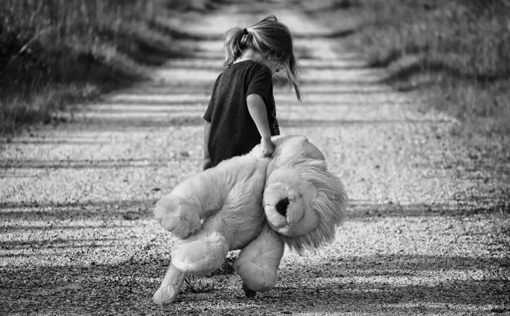 Black and white picture showing a little girl with a teddy. The girl moves in unknown direction along a country road. She looks lost and despaired. The picture symbolizes Bowlby’s concept of separation stress. John Bowlby was the key figure in the history of PTSD research