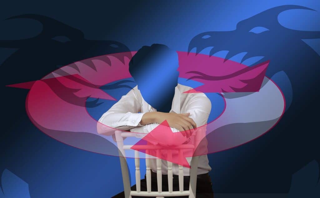 A man in a white shirt and black pants sitting backward on a white chair with his elbows resting on the back support. The background is blue and you can see a pink circle with arrows and behind it the faces of two dragons facing each other.  This represents addiction and the ongoing cycle that is broken with the help of addiction counseling and being in recovery.    