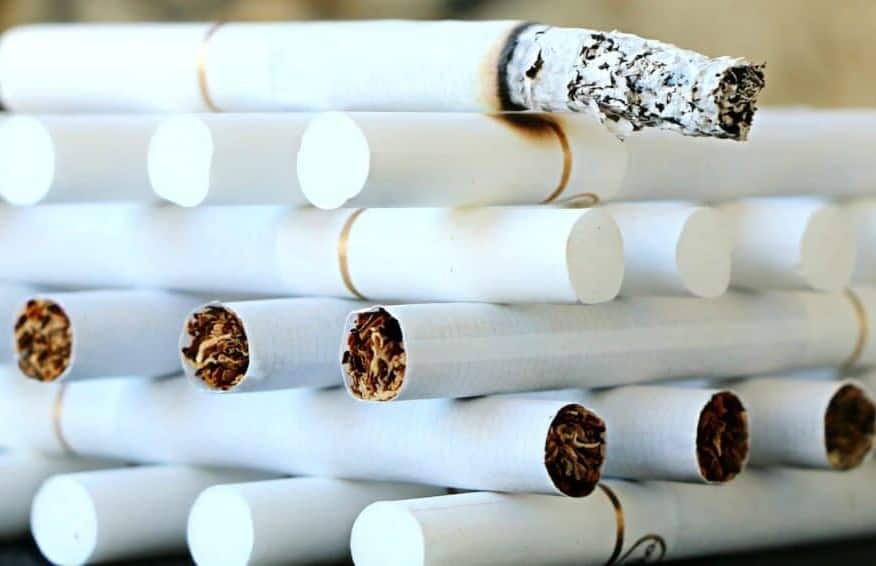 White filter cigarettes with a gold line around the base of the filter stacked like a grate.  At the very top a lit cigarette with ashes at the tip that is burning the cigarette below it.  This symbolizes the addictive nature of smoking and how a smoker goes from one cigarette to the next