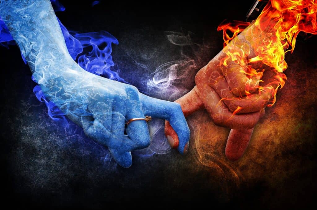 Marriage counselling. Two hands holding each other by a finger. The right hand is under fire, the left blue hand is wearing a ring and is surrounded by smoke