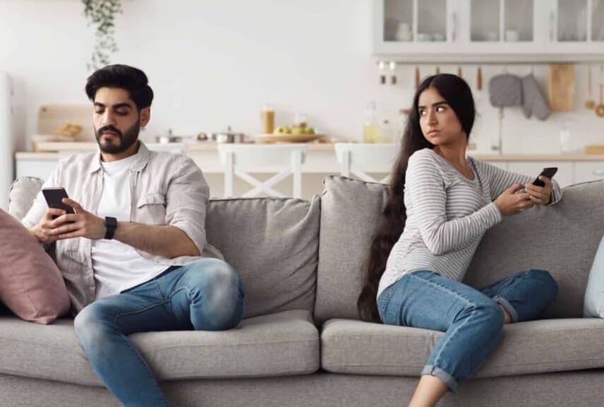 Marriage counselling. Man, and women sitting on the sofa. Both play with their mobiles. There is no interest for the partner. The woman looks angry at the man. The picture refers to marriage counselling