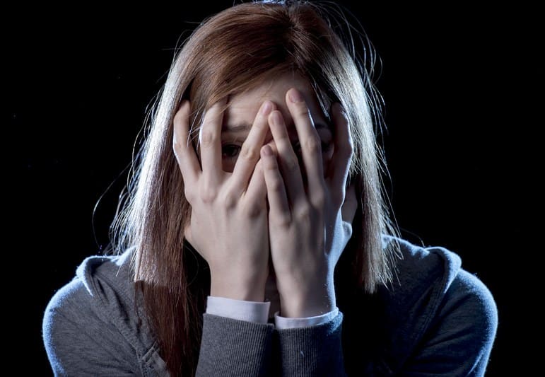 Anxiety disorders. The picture shows a young anxious girl covering her face with hands 