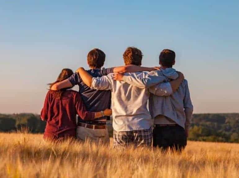 Alcohol dependency treatment. Four young people looking at the horizon and embracing each other standing in a cornfield. In front of them a blue sky. The picture shows people supporting each other in the alcohol dependency treatment