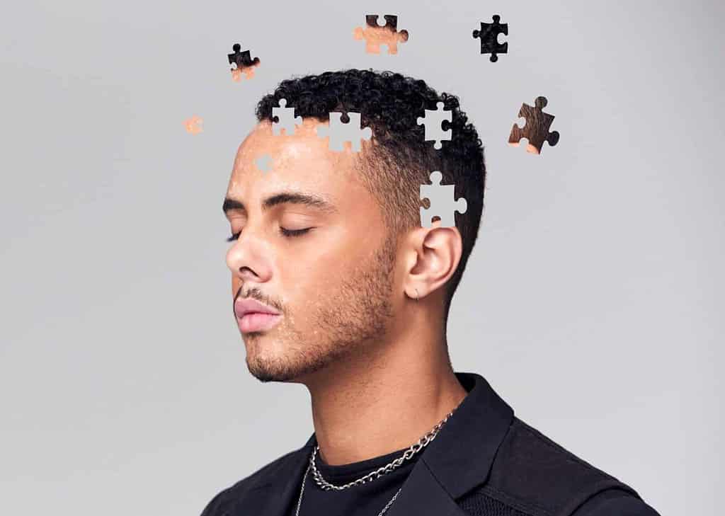 Causes of PTSD. The main role in the oset of PTSD play the trauma but there are many other factors triggering the disorder such as genetic, environmental, and psychosocial factors. The picture shows a young man whose head is fragmented like a puzzle  