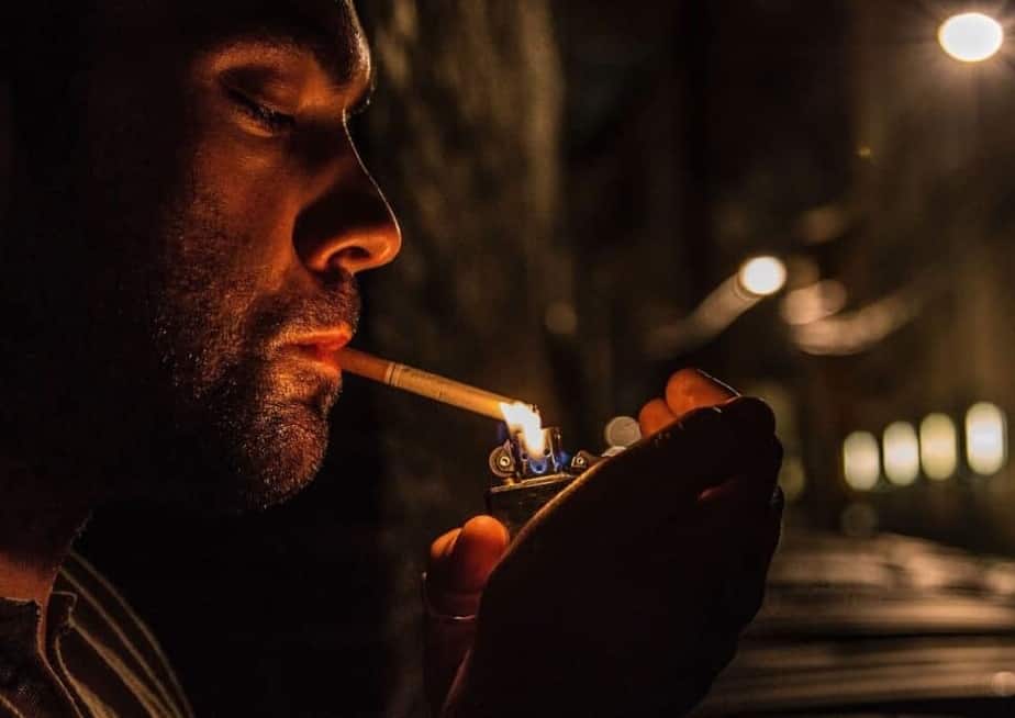 Quitting smoking with hypnosis. A night time scene where a man is lighting a cigarette outside a dimly lit city street.  It shows how a smoker is feeding his addiction. A night time scene where a man is lighting a cigarette outside a dimly lit city street.  It shows how a smoker is feeding his addiction.   