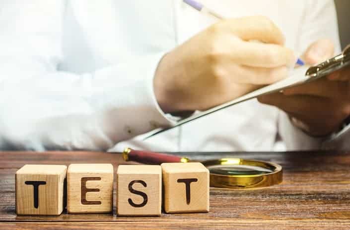 Psychometric testing in Dubai. The picture shows a person holding a note and a pen, sitting behind a wooden desk. On the desk we see a magnifying glas and wooden cubes with the inscription: "test". 