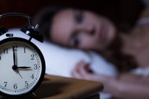 A women not able to sleep with a clock in the foregrouns. Sleeplessness and its causes