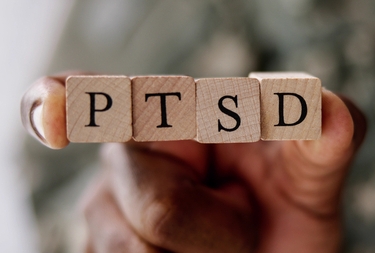 Post-traumatic stress disorder can be triggered by an accident, an act of violence, or another life-threatening event. The picture shows 4 cubes with the inscription "PTSD." The picture related to the topic of this article about causes and risk factors for PTSD.